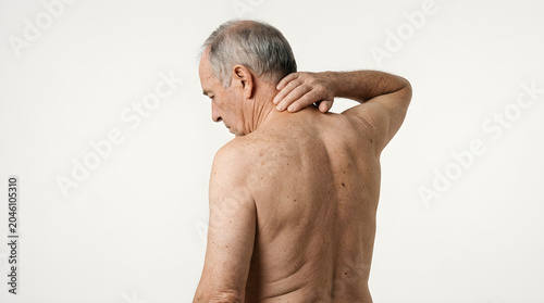 An older man with gray hair touches his painful neck while experiencing discomfort in his upper back and shoulders