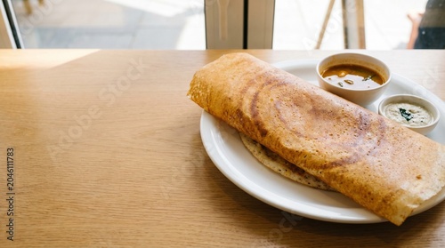 Crispy masala dosa served with sambar and coconut chutney on a white plate on a wooden table