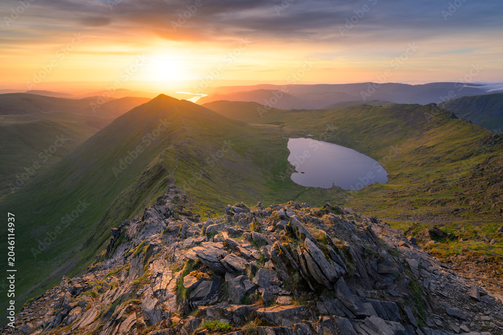 Fototapeta premium Golden sunrise seen from Helvellyn overlooking spectacular view of Swirral Edge, Red Tarn and Ullswater in The Lake District mountains.