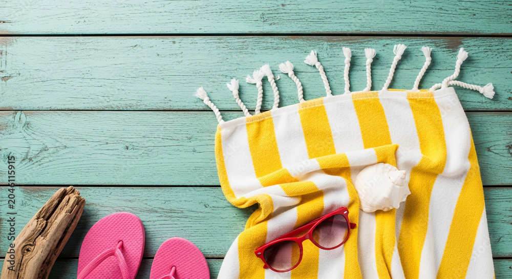 Obraz premium Beach towel, flip-flops, sunglasses, and driftwood on a teal wooden background, symbolizing summer vacation and relaxation