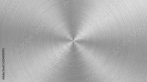 A polished metal surface displays concentric circles radiating from a central point. The metal exhibits a brushed texture, creating a subtle gradient of light and shadow.