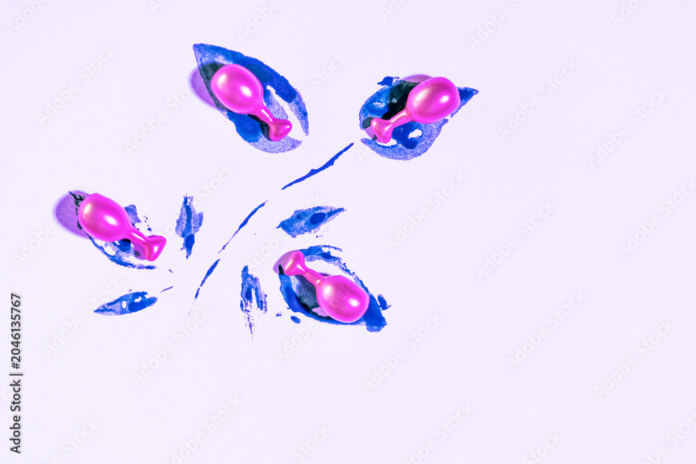 Obraz premium Minimalist composition of vibrant pink cosmetic capsulas nestled in deep blue textured paint strokes on a light lavender background. .