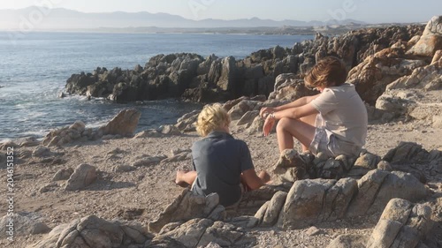 2 pre teen boys climbing and exploring the rocky coastline of DeKelders, South Africa