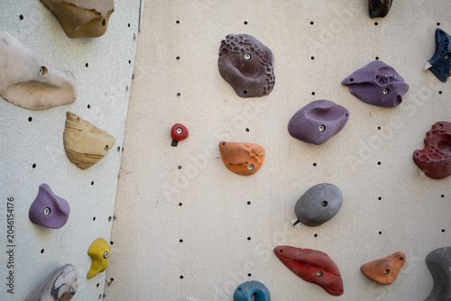 Colorful climbing holds on a beige indoor climbing wall, bouldering gym background