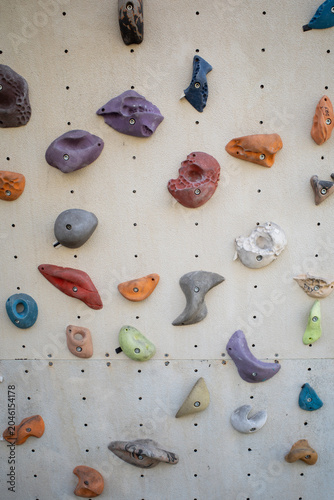 Colorful climbing holds on a beige indoor climbing wall, bouldering gym background