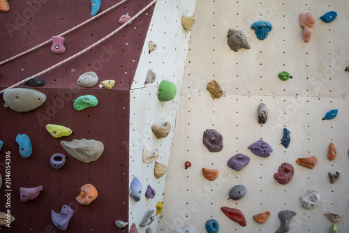 Colorful climbing holds on a beige and burgundy indoor climbing wall, bouldering gym background