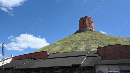 Gediminas' Tower, a Historic Landmark of Vilnius, Lithuania, Stands Tall on a Green Hill Against a Clear Blue Sky with Fluffy White Clouds on a Sunny Day.