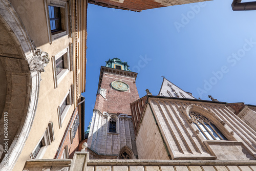 View of a tall clock tower rising above old buildings under a clear blue sky in a historic city. Wawel Royal Castle in Krakow