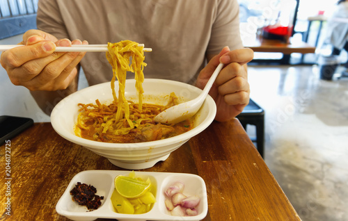 A person using chopsticks to eat Thai northern style chicken curry noodle soup, Khao Soi, at a restaurant table.