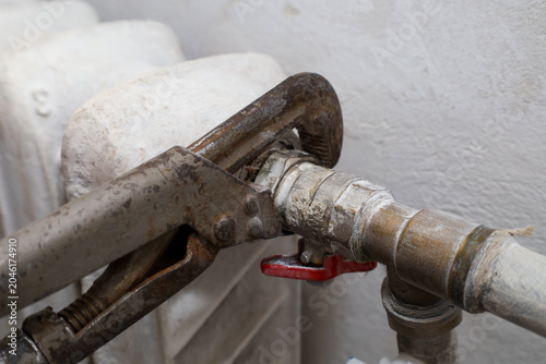 Billede på lærred An old rusty pipe wrench securely grips a metal fitting of a heating radiator to perform repair work