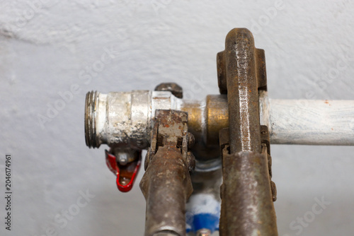Fotografi An old rusty pipe wrench firmly grips a metal coupling with a red lever to perform plumbing repairs