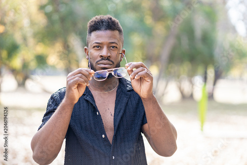 Stylish Black Man Holding Sunglasses Outdoors with a Confident Gaze