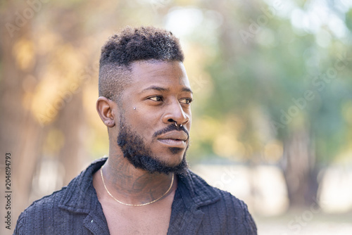 Stylish Black man with beard and nose ring looking away outdoors
