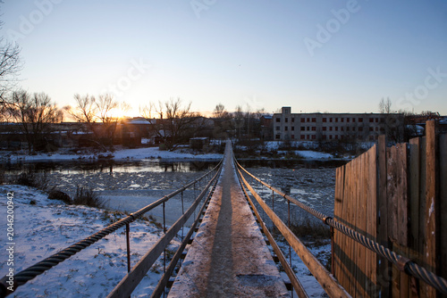 A suspension bridge over the Msta River in winter, on a sunny day. Borovichi, Novgorod Oblast, Russia.