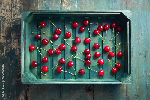 Fresh red cherries scattered in a rustic wooden crate on vintage wooden background.