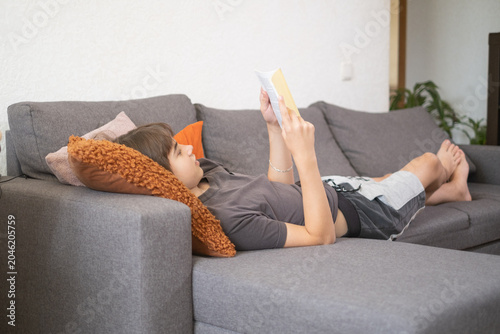 Foto Teenager reads a book on a couch in a living room during the afternoon at home,