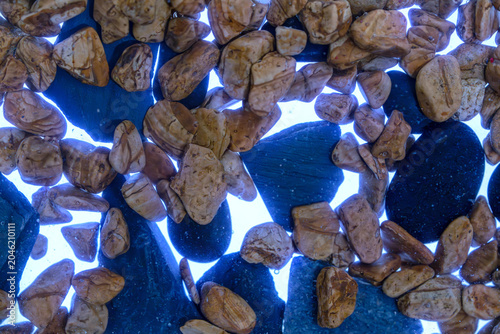 Canvas Print Wet pebbles and stones submerged in water with strong backlighting creating an a