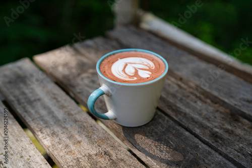 A cup of cappuccino coffee featuring latte art served on a rustic wooden table in a cozy cafe setting.
