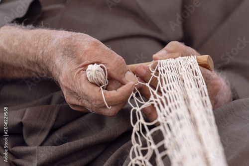 Old man is knitting traditional fishing net, hands in frame. UAE heritage