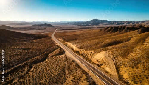 Scenic desert highway stretching towards distant mountains under a clear blue sky.