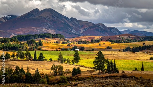 Scenic Landscape of Fields and Mountains Under Cloudy Skies.