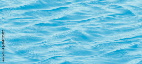 Quadro su tela Blue sea water ripples background with soft sunlight and small waves creating pe