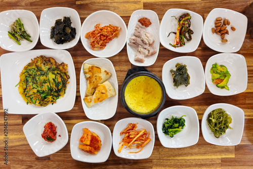 Traditional Korean set meal with assorted side dishes steamed egg grilled fish pancakes vegetables and pork served on a wooden table showcasing authentic Korean dining culture.