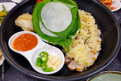 Traditional Korean bossam set meal with boiled pork slices, soybean paste stew, fresh vegetables, kimchi, rice, and assorted side dishes served on a dining table.
