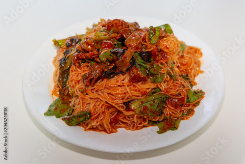 Spicy golbaengi somyeon with seasoned sea snails, fresh vegetables, and thin wheat noodles mixed in a savory Korean red pepper sauce on a white plate.