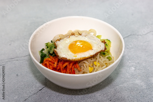 Traditional Korean bibimbap topped with fried egg, bean sprouts, vegetables, and seasoned side ingredients served in a white bowl on a clean background.