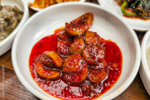 Traditional Korean pickled plum side dish served in spicy red seasoning sauce, showcasing authentic Korean preserved food and homemade banchan culture.