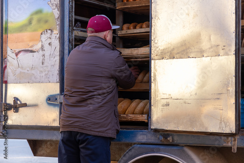 Tablou pe pânză A delivery driver loads fresh bread loaves into metal shelves of a truck, convey