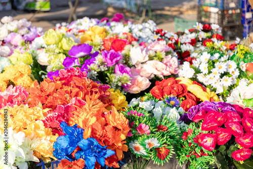 Vibrant assortment of artificial flowers in a variety of bright colors displayed at an outdoor market stall, capturing a cheerful and seasonal atmosphere for home decor and design