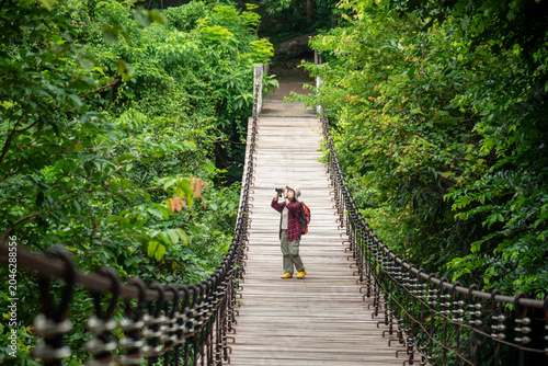 Female Hiker Observing Wildlife With Binoculars On A Wooden Suspension Bridge In A Tropical Forest