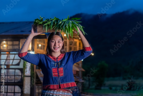 Smiling Young Woman In Traditional Indigenous Textiles Carrying A Basket Of Fresh Organic Vegetables At Twilight
