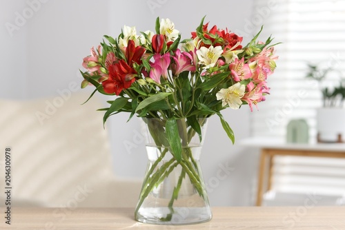 Bouquet of alstroemeria flowers in vase on wooden table at home