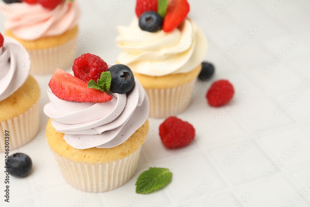 Obraz premium Yummy cupcakes with fresh berries and mint on light tiled table, closeup. Space for text