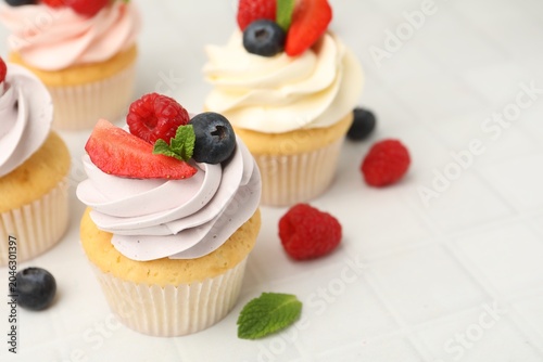 Yummy cupcakes with fresh berries and mint on light tiled table, closeup. Space for text