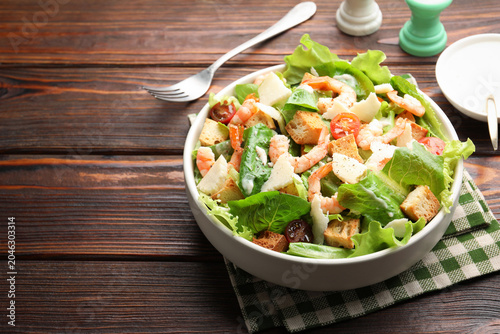 Bild auf Leinwand Delicious Caesar salad with shrimps in bowl served on wooden table, closeup