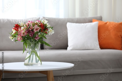 Bouquet of beautiful alstroemeria flowers in glass vase on white table at hom...