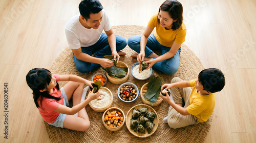 Family sitting together wrapping traditional zongzi with ingredients and bamboo leaves