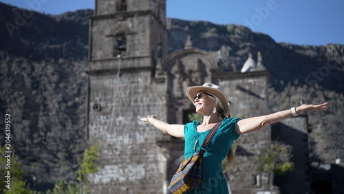 Foto Mature woman stands with arms open at San Javier Mission, feeling the joy of exp