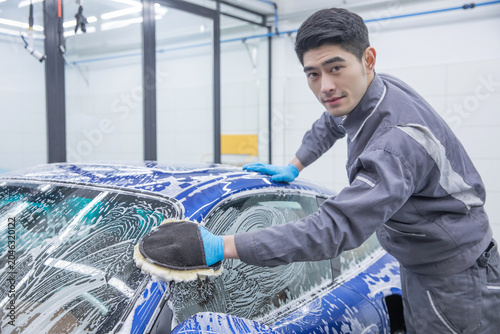 Photos Car wash worker scrubbing soapy blue vehicle in cleaning bay