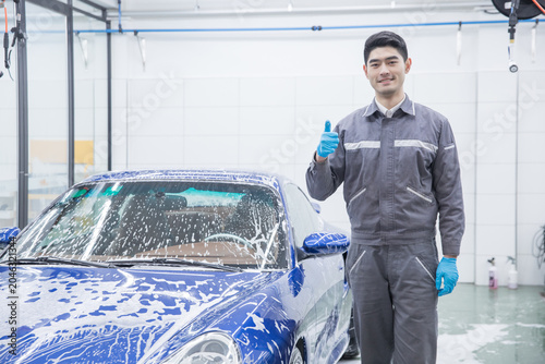 Fotografía Car wash worker giving thumbs up beside soapy blue car in garage