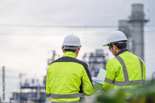 Two industrial engineers using a laptop for site inspection and planning at a modern power plant facility. Professional technicians discussing project operations and factory maintenance.