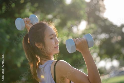A woman is lifting dumbbells in a park and exercising.