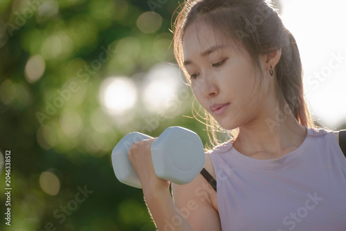 A woman is lifting dumbbells in a park and exercising.