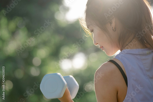 A woman is lifting dumbbells in a park and exercising.