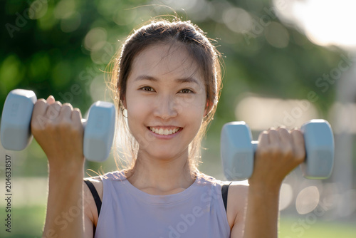 A woman is lifting dumbbells in a park and exercising.