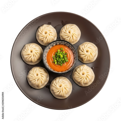 Steamed momos arranged in a circle on a dark plate with a small bowl of spicy orange dipping sauce and green... isolated on a transparent background